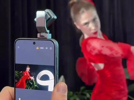 上手体验一下荣耀Robot手机~
在今年的MWC 2026展会上,如果说有一台机器让我排队排了半小时也要摸到真机,那一定是荣耀带来的这个“新物种”——荣耀Robot Phone。在来巴塞罗那之前,我以为它只是个概念噱头,但真正把玩之后,我只想说:手机还能这么玩?
当把这台银灰色的机器拿在手里,第一感觉是既熟悉又陌生。它的边框采用了拉丝装饰,整机质感在线,握在手里与普通的旗舰手机无异 。
但当你翻到背面,视线就再也移不开了——那个硕大的、有点像大疆Osmo Pocket的三轴云台相机,就这么明晃晃地镶嵌在机身顶部 。它并不突兀,反而带着一种“理工男”式的机械美感,背面的“α”Logo似乎在低调地告诉你:这家伙不简单 。
上手的第一件事,当然是滑动那个隐藏的开关。随着一声清脆的机械音,顶部的玻璃门滑开,那颗摄像头模组通过机械臂完成了一个漂亮的“后空翻”,直接从后置形态转为独立的云台 。
我试着拿着它走动,正如之前网上爆料的那样,它的360°机械云台真的做到了“如影随形” 。我在展台前左右移动、小跑两步,取景框里的画面始终牢牢锁定我的脸,稳得像贴在了三脚架上 。这种体验,确实解决了我们平时拍Vlog时最头疼的问题:手抖、构图歪、人跑出画面。难怪有人说,这相当于“在手机上装了个大疆” 。
但最让我惊讶的,还不是拍照。现场工作人员演示了AI智能体模式。当我对着手机说话时,它顶部的云台就像小动物的脑袋一样,随着我的移动而转动,“目光”一直追随我 。播放音乐时,它甚至会随着节奏轻轻律动。更可爱的是,屏幕上的小人表情会根据对话内容作出反应,甚至在你下达指令时,它还会像听懂了一样“点点头” 。
这种交互感,打破了以往我们对手机冰冷的认知。它不再是你戳一下它才动一下的工具,而是像一个能听懂话、有情绪的数字伙伴 。
荣耀Robot Phone确实做到了让人眼前一亮。 在智能手机同质化严重的今天,荣耀敢于把机器人的“身体”和AI的“大脑”塞进手机里,这本身就是一件很酷的事 。
如果你受够了每年千篇一律的旗舰机,渴望一点新鲜感,那么这台会“点头”、会“跳舞”、能自己追着你拍的Robot Phone,或许就是你在寻找的下一部“梦中情机”。它不仅是手机,更是目前我们能买到的、最具未来感的AI终端之一 。#荣耀Robot