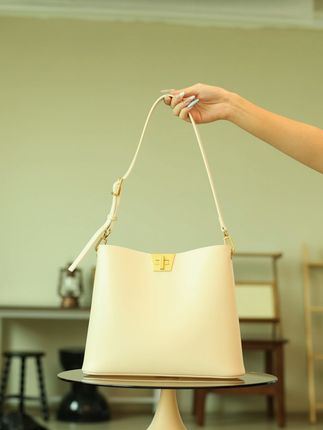 奶白水桶包:金扣复刻时光韵味 奶白漆皮如陈酿初雪,泛温润柔光,触手柔韧挺括。金色几何扣似时光徽章,轮廓复刻复古腔调,扣合轻响是仪式注脚。水桶型包容日常:通勤装文件、约会盛花束,肩带可调节适配多元风格。漆皮随使用沉淀光泽,金扣始终锃亮,二者对话时光,让复古高级融入日常呼吸。#手提包 #水桶包 #大容量包包 #设计感包包