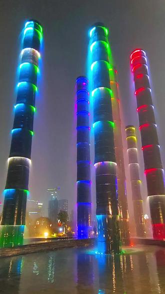 成都SKP的“生机之塔”是商场最具标志性的景观装置,以其独特的设计与梦幻的光影效果,成为成都新晋的网红打卡地标。这座艺术水柱由六根金属铝材质的立柱组成,三根高39米,三根高26米,形似竹节,寓意“节节高升”。水流自上而下流淌,象征“天府之国,天上来水”,暗合“水生财”的文化意象,也呼应了成都作为“天府之国”的生态底蕴。每根水柱皆有独特寓意,分别代表“福、财、爱、健康、智慧、美”,将传统文化与现代商业精神巧妙融合。 塔身配备5328个喷嘴与环形彩灯,夜间开启灯光秀时,呈现“七彩渐变、闪动跳跃、环状灯带、同色灯光”四种模式,每4分钟循环一次,水雾与光影交织,营造出如梦似幻的赛博诗意氛围。尤其在夜晚,霓虹灯光映照下,水柱宛如流动的星河,与远处环球中心的灯火遥相呼应,成为成都夜景的“天花板”级景观。阳光充足时,水雾中更易形成彩虹,为打卡增添一抹自然奇迹。夜游skp生机塔随拍#成都skp #成都skp生机之塔 #生命之水#美丽夜景太迷人 #随拍记录生活