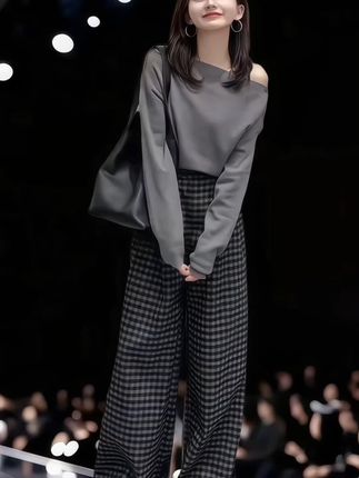 单肩上衣,领口设计为斜肩款式,露出一侧肩头,显得优雅又性感。下装是一条黑灰格纹阔腿裤,图案经典且富有复古魅力,与灰色上衣形成和谐的搭配。她的脚上穿着一双浅棕色的平底鞋,增添了一丝休闲与柔和的气息。#秋冬穿搭新鲜感在线 #小个子秋冬穿搭 #女性穿搭 ##秋季日常实用穿搭思路分享